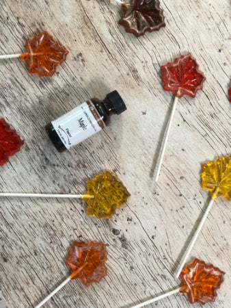 Maple syrup lollipops on a wooden surface with a 1 oz bottle of maple super strength flavoring.