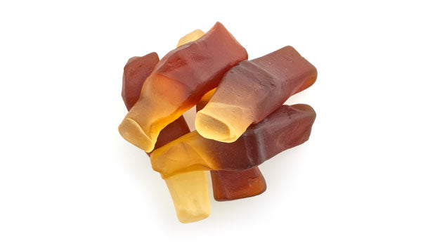 Stack of chewy, multicolored gummy cola bottles on a white background