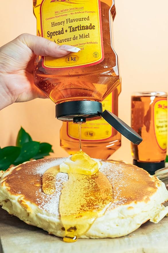 Honey being drizzled onto pancakes from a honey dispenser.