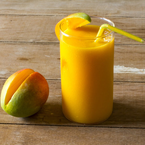 Mango Slushie in a glass cup and yellow straw on a wooden table with a piece of mango fruit next to it by Rubicone Canada