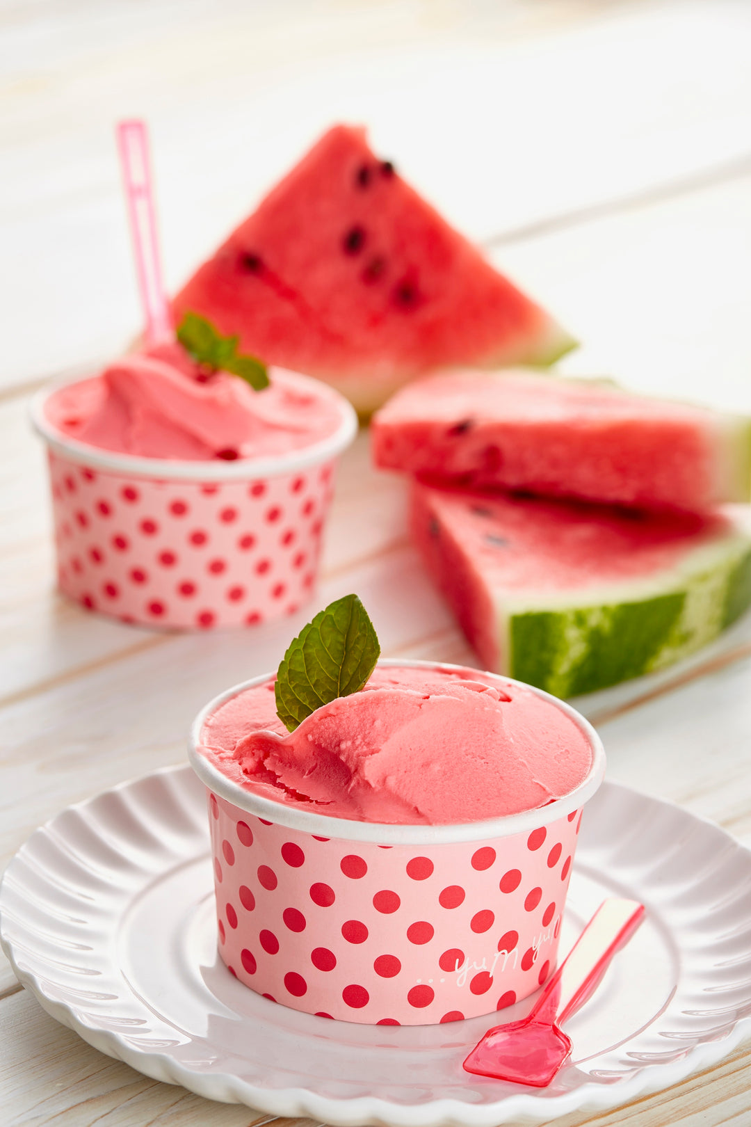 Watermelon gelato ice cream in a pink polka dot cup with watermelon slices in the background