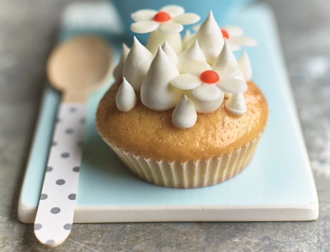Cupcake with white frosting flowers on a blue plate with a wooden spoon.