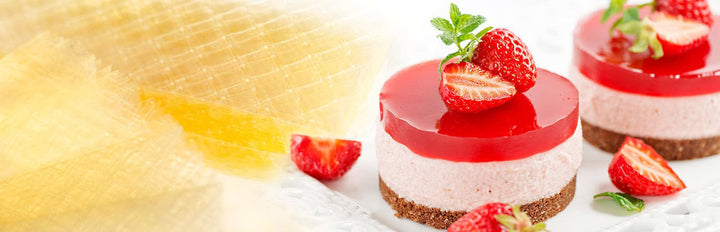 Two small dessert cakes with red and white layers and strawberries on top, placed on a white surface.