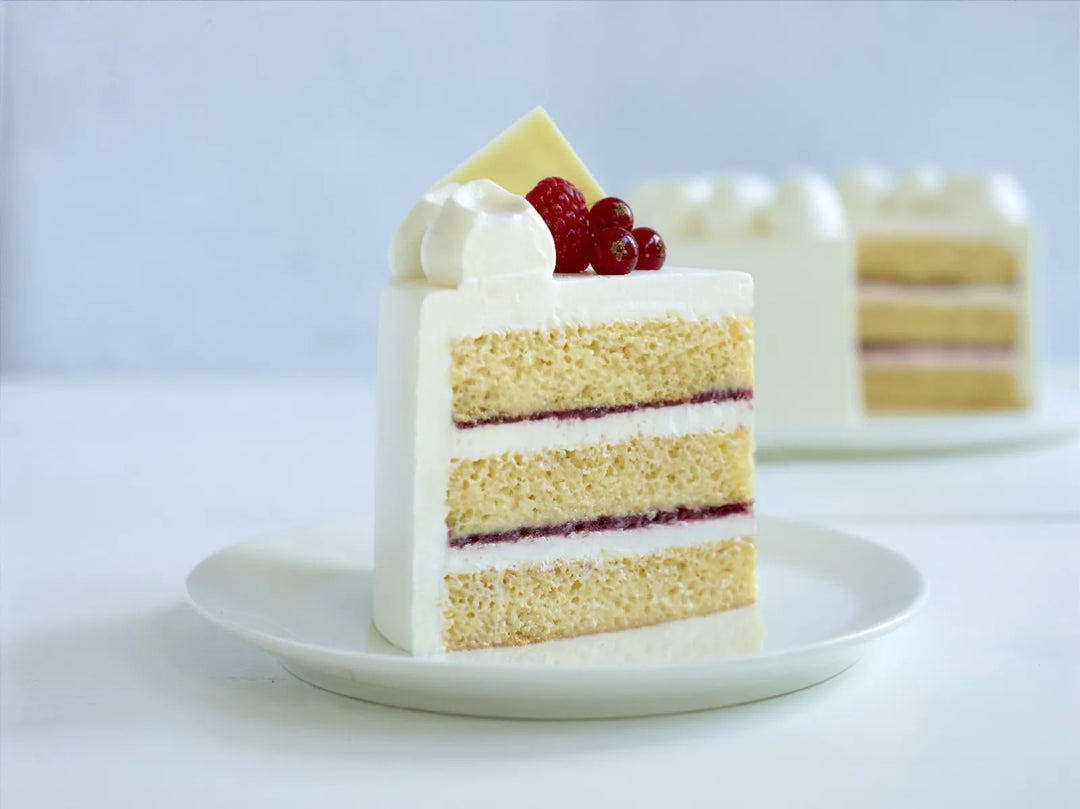 Slice of layered cake with white non-dairy plant-based frosting and red berries on a white plate.