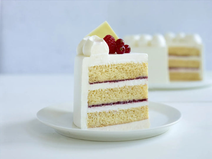 Slice of layered cake with white non-dairy plant-based frosting and red berries on a white plate.