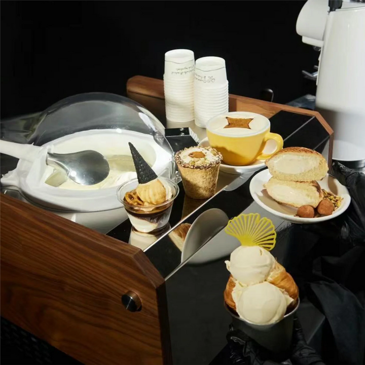 Dessert display with ice cream, pastries, and coffee on a reflective surface.
