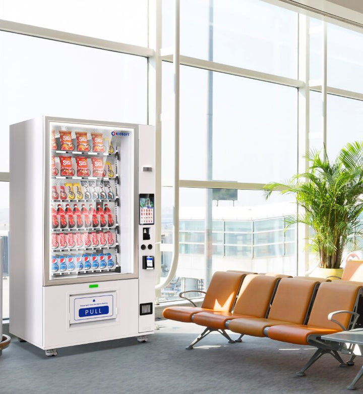 Vending machine in a modern waiting area with large windows and orange chairs.